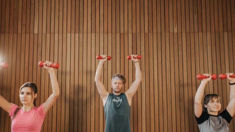Three adults exercising with dumbbells in fitness class, promoting a healthy lifestyle.