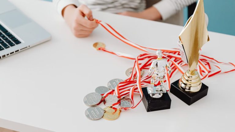 Young person displays football trophies and medals on a desk, showcasing athletic pride.